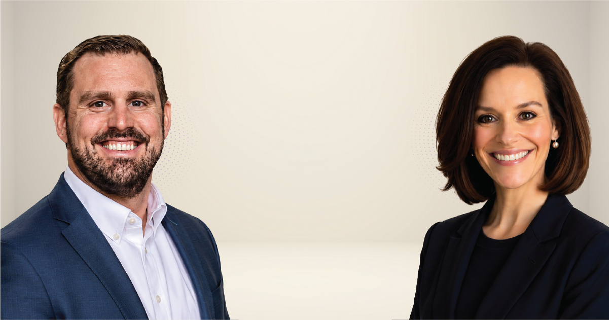Two smiling professionals stand side by side in a neutral studio backdrop, dressed in business attire (man in blue blazer, woman in dark blazer).