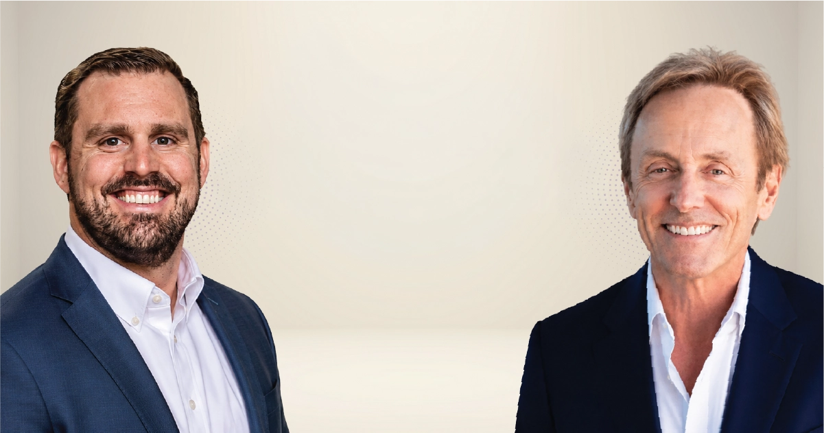 Two men in business suits smiling at the camera, standing against a light neutral backdrop.