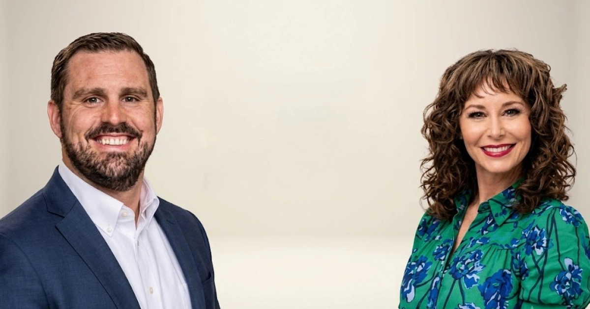 Two smiling professionals pose for a portrait: man in a blue suit on the left and woman in a green floral blouse on the right.