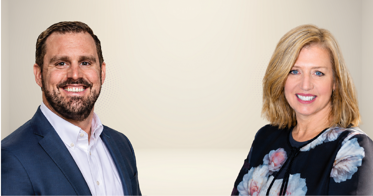 Two smiling professionals, a man in a navy blazer and white shirt and a woman in a floral blouse, stand side by side against a light background.